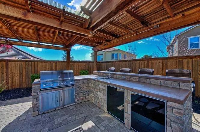 Outdoor kitchen with a built-in stone grill, spacious countertops, and a wooden pergola for shaded outdoor gatherings.