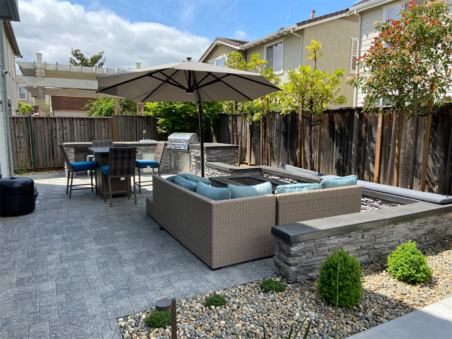Large backyard patio with gray pavers, outdoor seating, and a built-in fire pit, by a top paver contractor in Vacaville, CA.