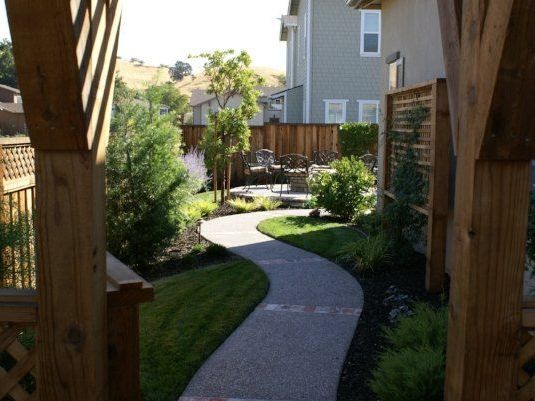 Curved pathway leading to a cozy patio, with lush plants and a pergola by Turfworks Inc, landscape company in Vacaville, CA.