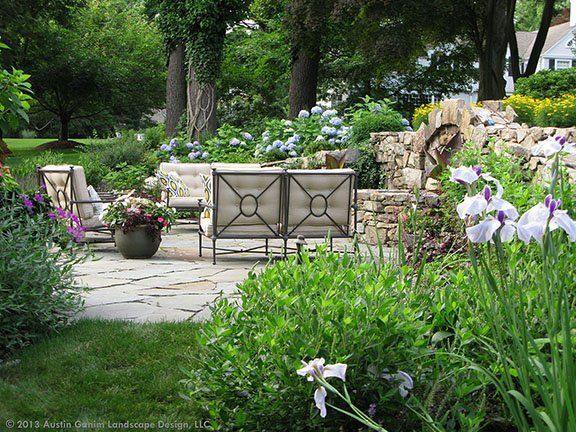 A landscape design in Davis, CA in a garden with a patio and chairs surrounded by flowers and trees.