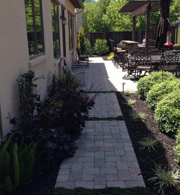 A brick walkway leading to a patio with tables and chairs | Paver Contractor in Davis, CA