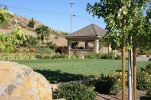 Beautiful landscape design in Vacaville, CA, with lush green grass, plants, trees, and a lovely gazebo in a scenic setting.