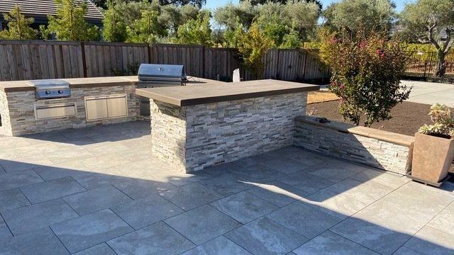 A large outdoor kitchen with a grill and fence, showcasing stunning landscape design in Vacaville, CA, by Turfworks Inc.