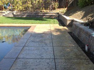 A concrete walkway leading to a pool in a backyard designed by Turfworks, Inc., the leading paver contractor in Vacaville, CA