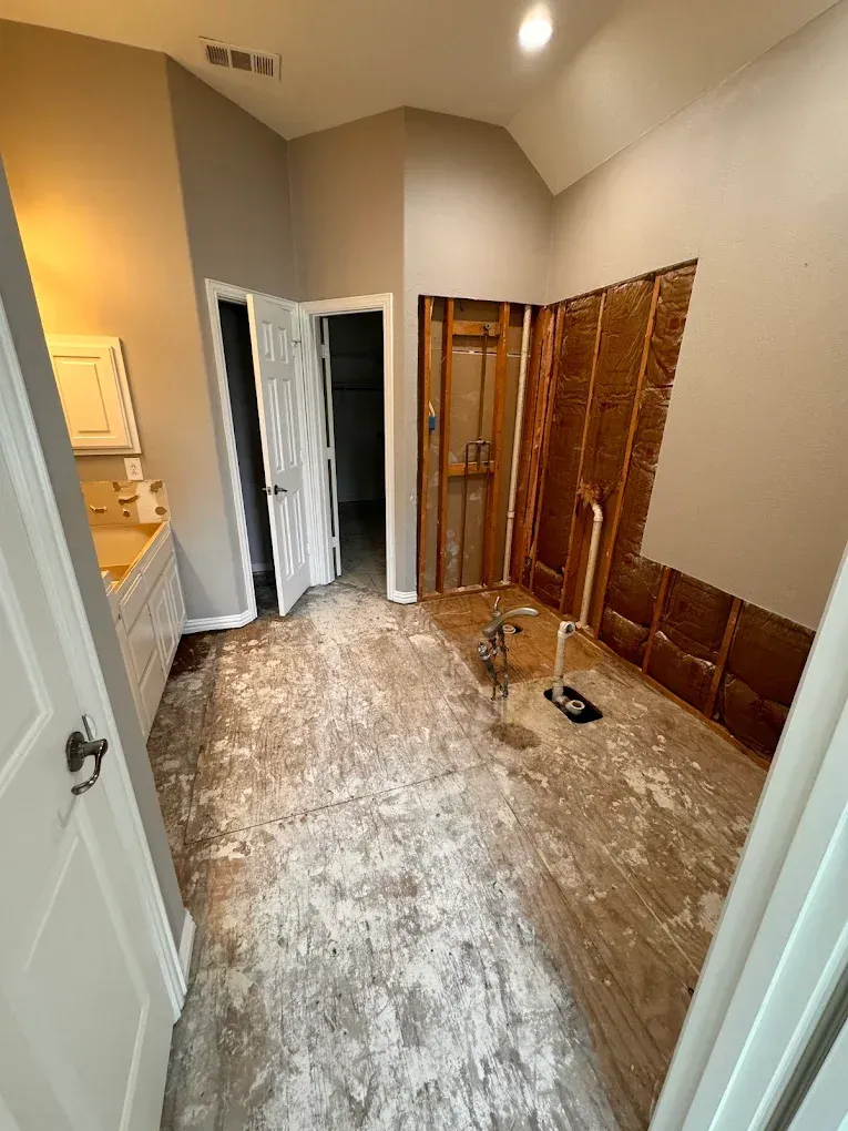 Bathroom under renovation; exposed walls, damaged floor, open doorway to another room.