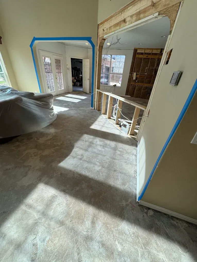 Interior view of a room under renovation. Light flooring, exposed framework, doorways, and blue painter's tape.