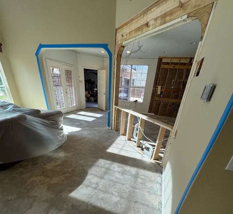 Room under renovation with a new arched doorway. Blue tape lines walls.