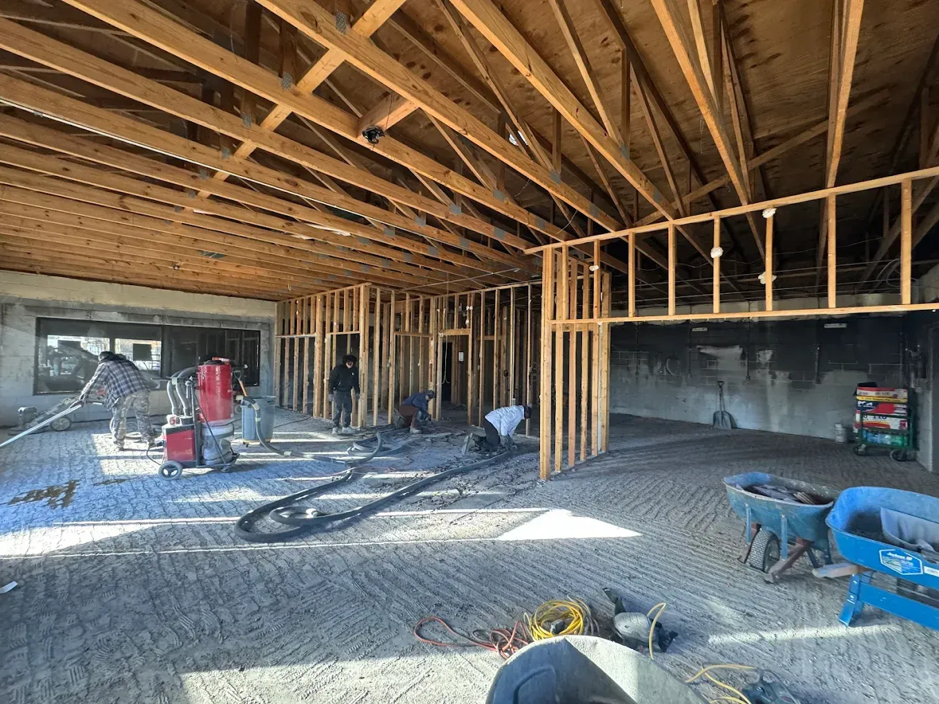 Construction site interior: workers, wood framing, concrete floor, beams, and tools.