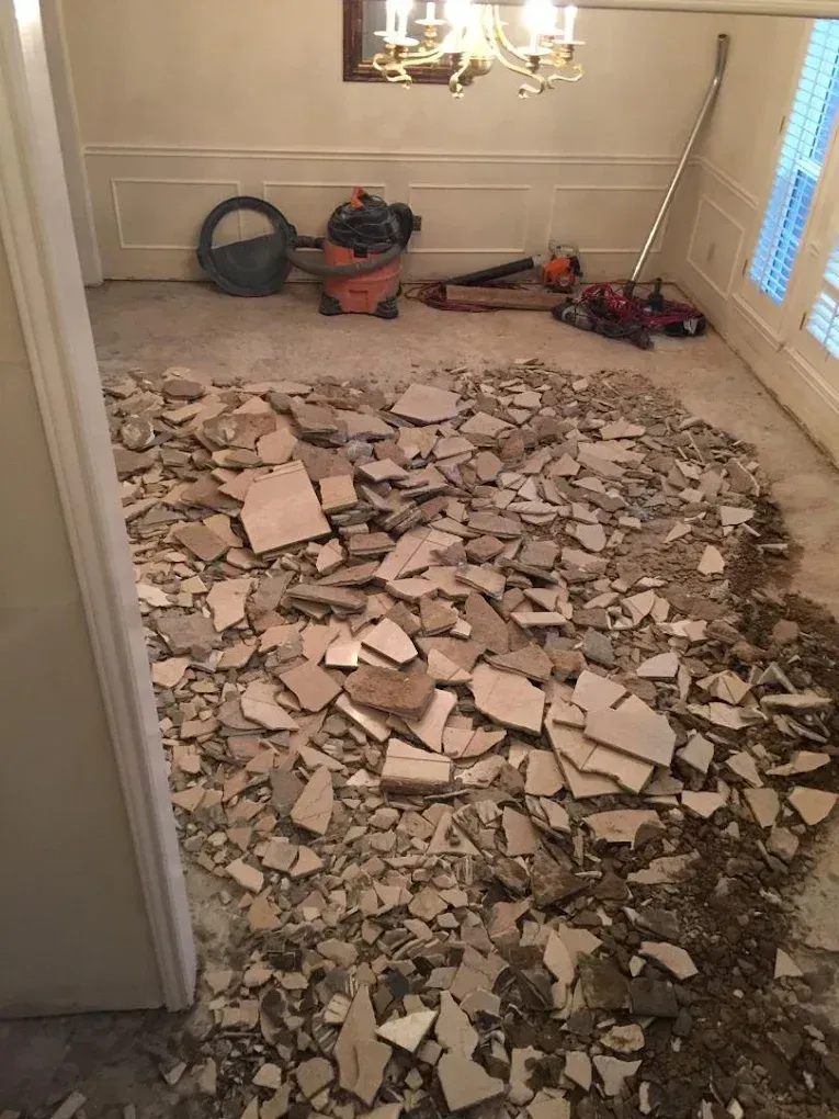 Room with tile demolition debris, vacuum, and tools on the floor.