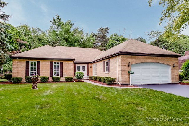 A large brick house with a white garage door and a large lawn in front of it.