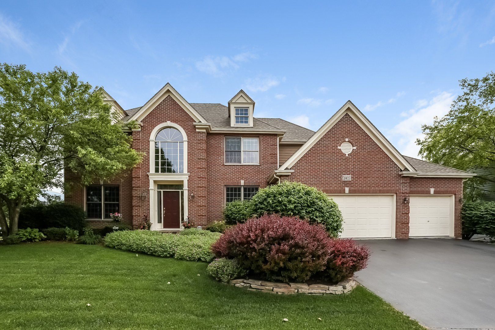 A large brick house with two garages and a lush green lawn.
