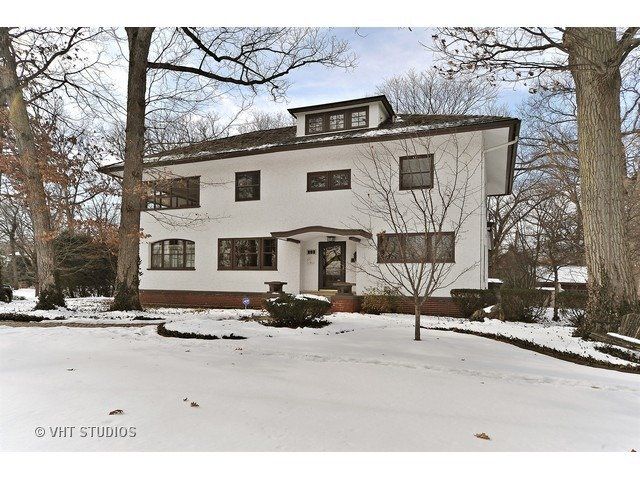 A large white house is surrounded by snow and trees