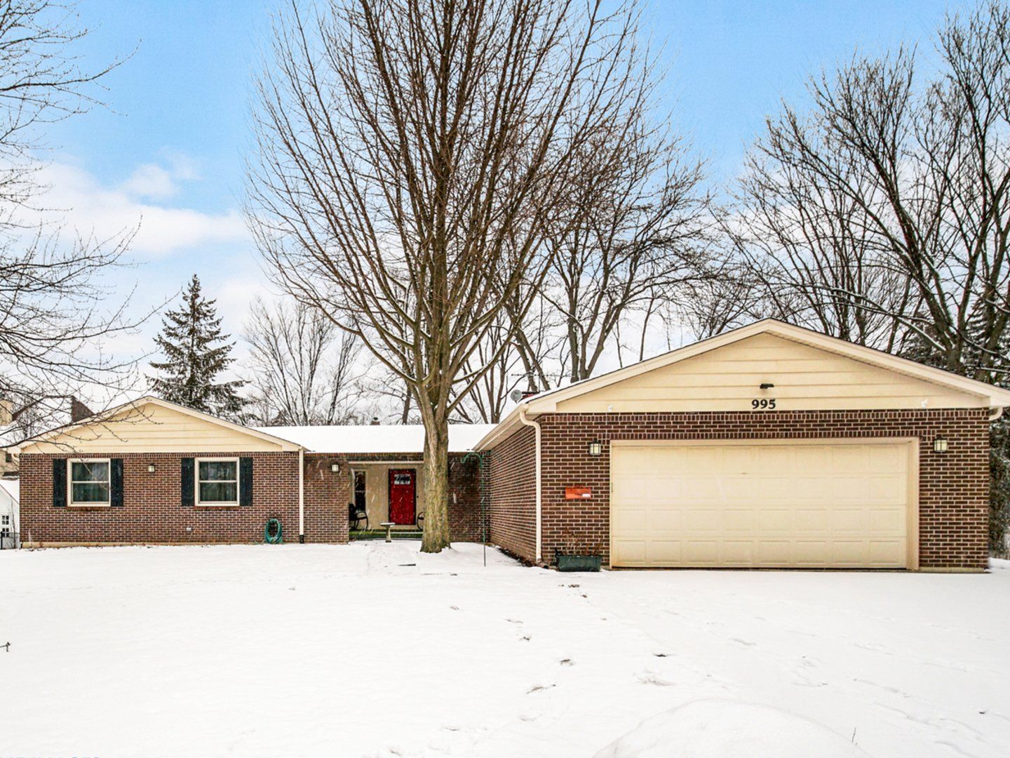 A brick house with a garage and a tree in the snow.