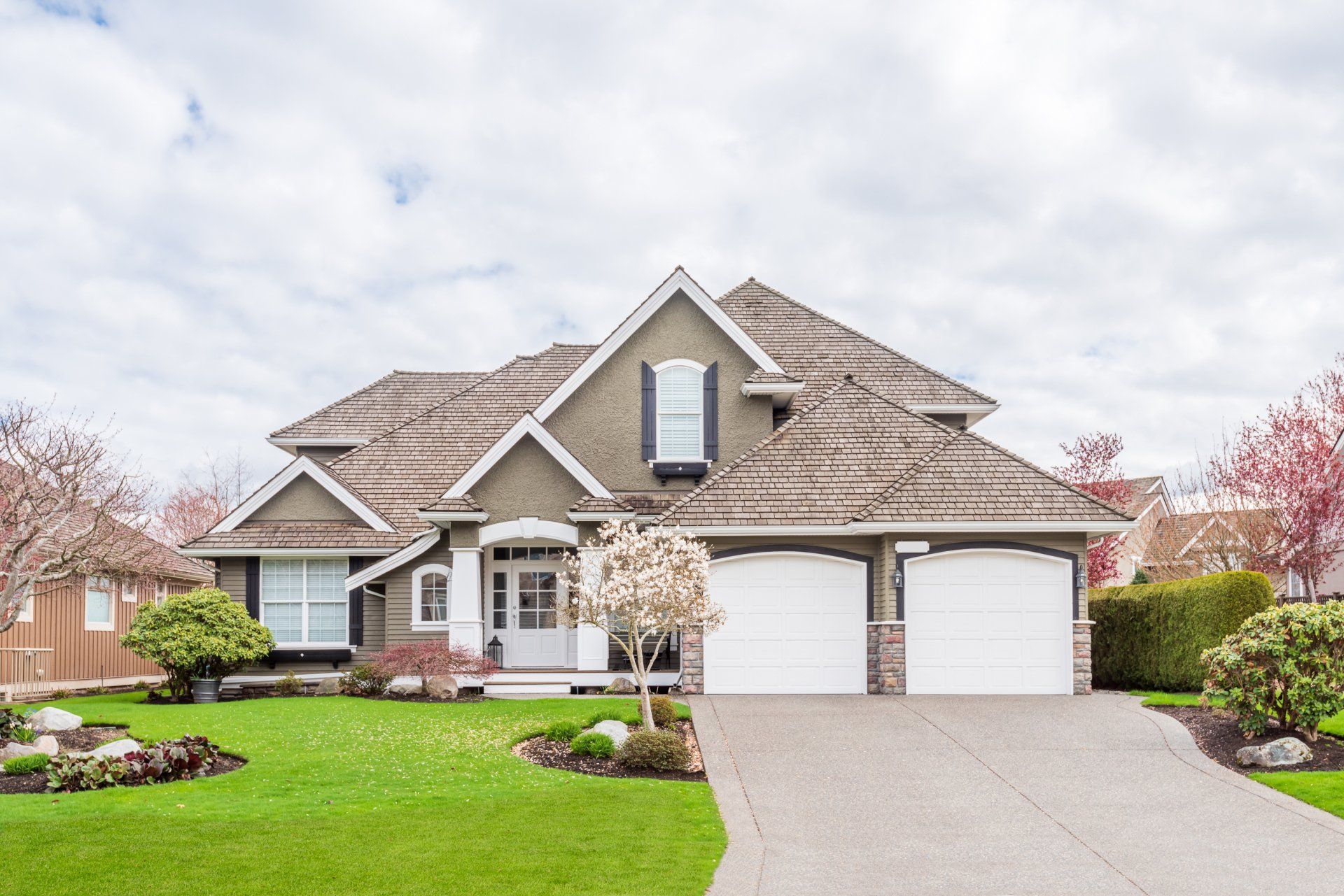 A large house with two garage doors and a lush green lawn.