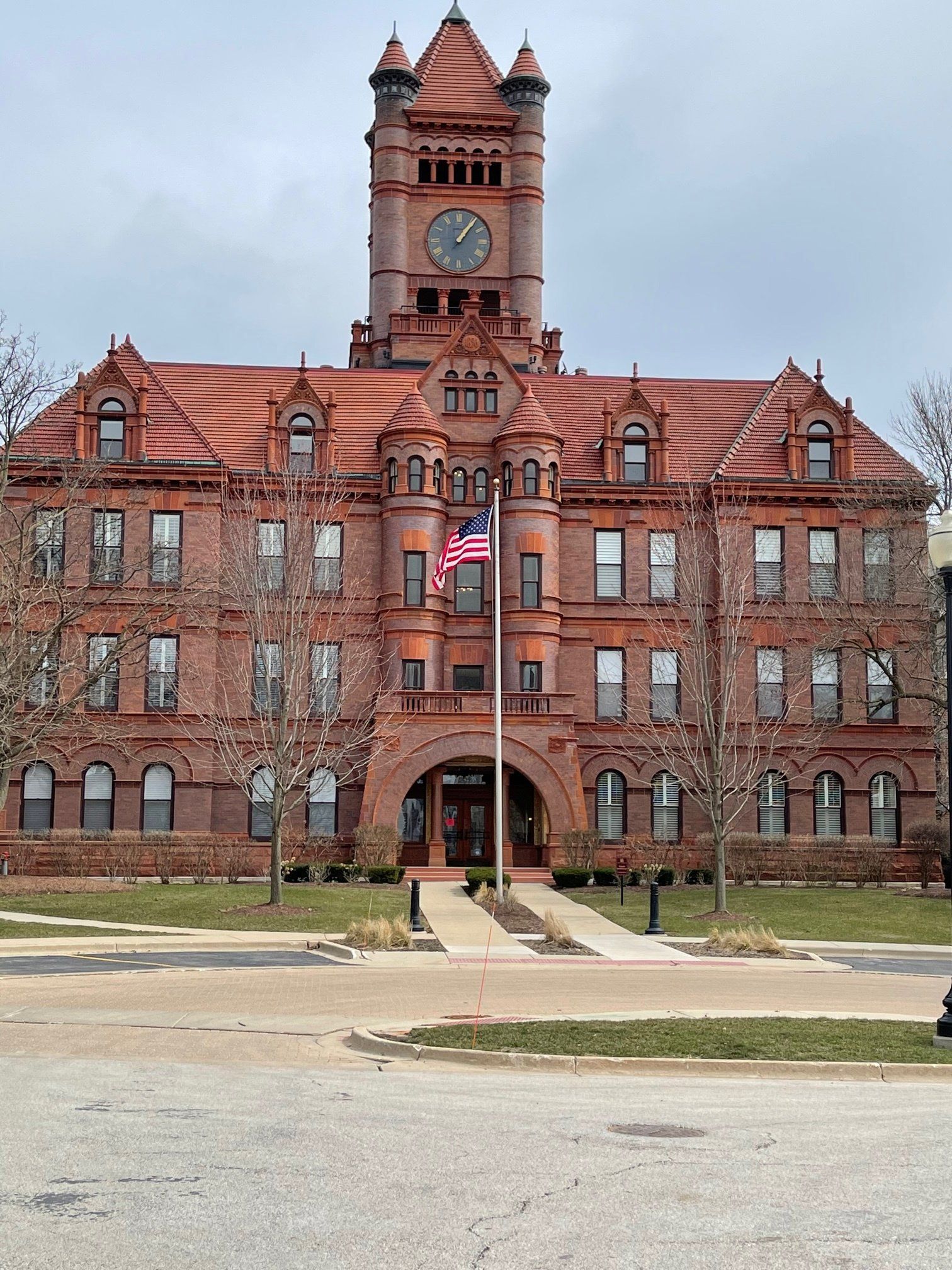A large red brick building with a clock tower and an american flag in front of it