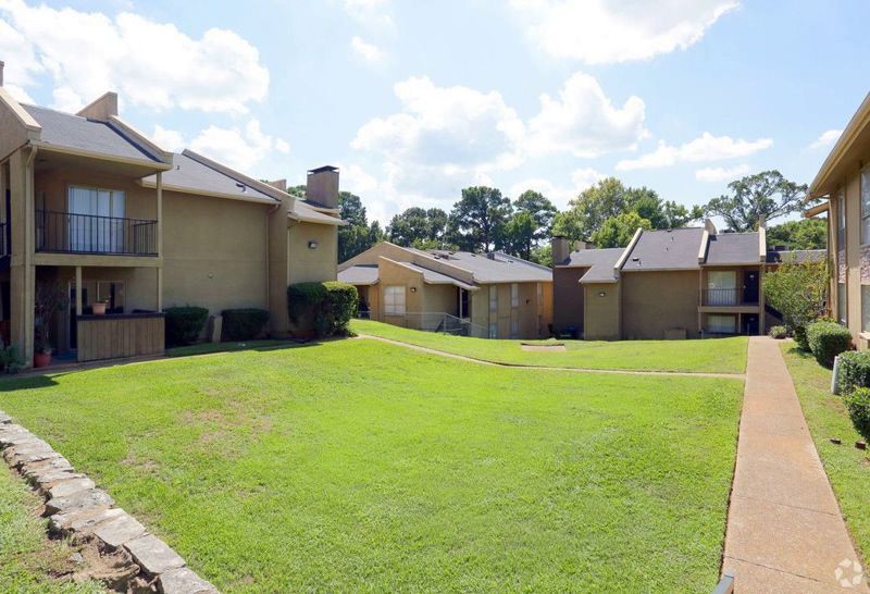 Apartment complex with beige buildings and a grassy courtyard on a sunny day.