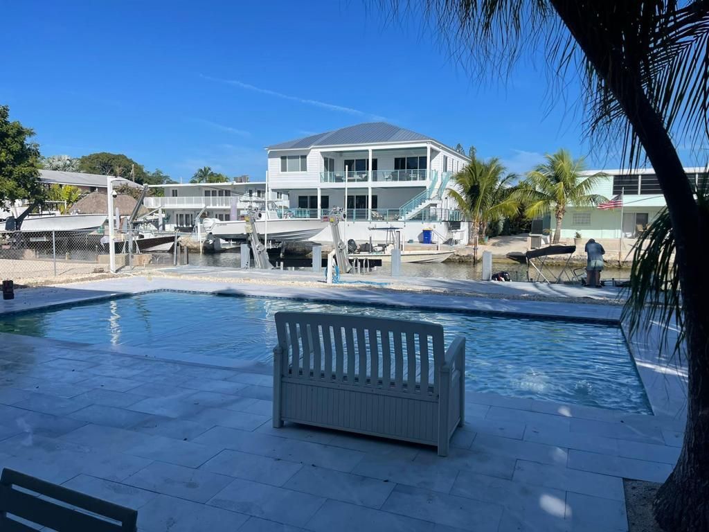 A swimming pool with a bench in front of it and a house in the background.