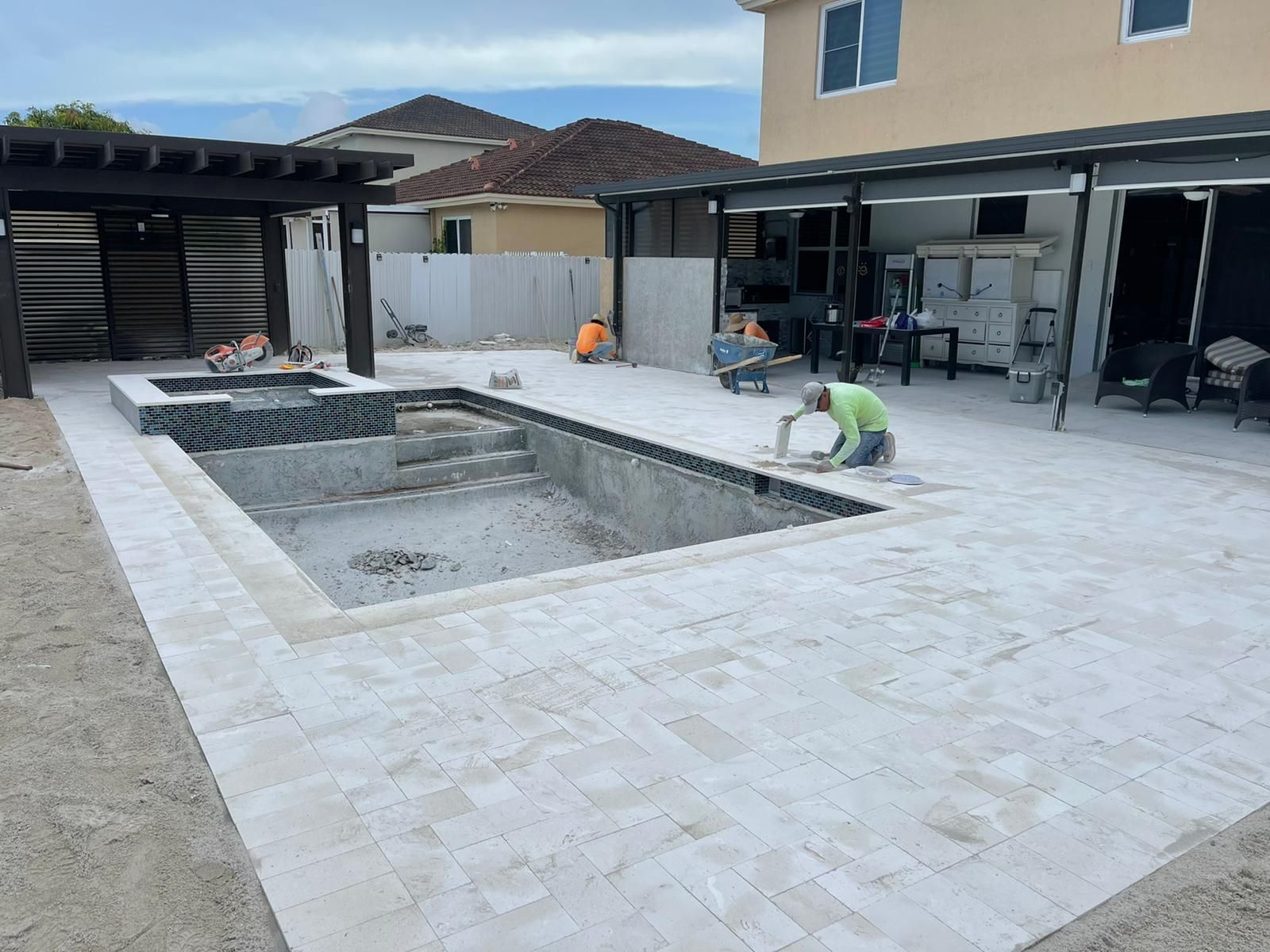 A man is working on a patio next to a swimming pool.