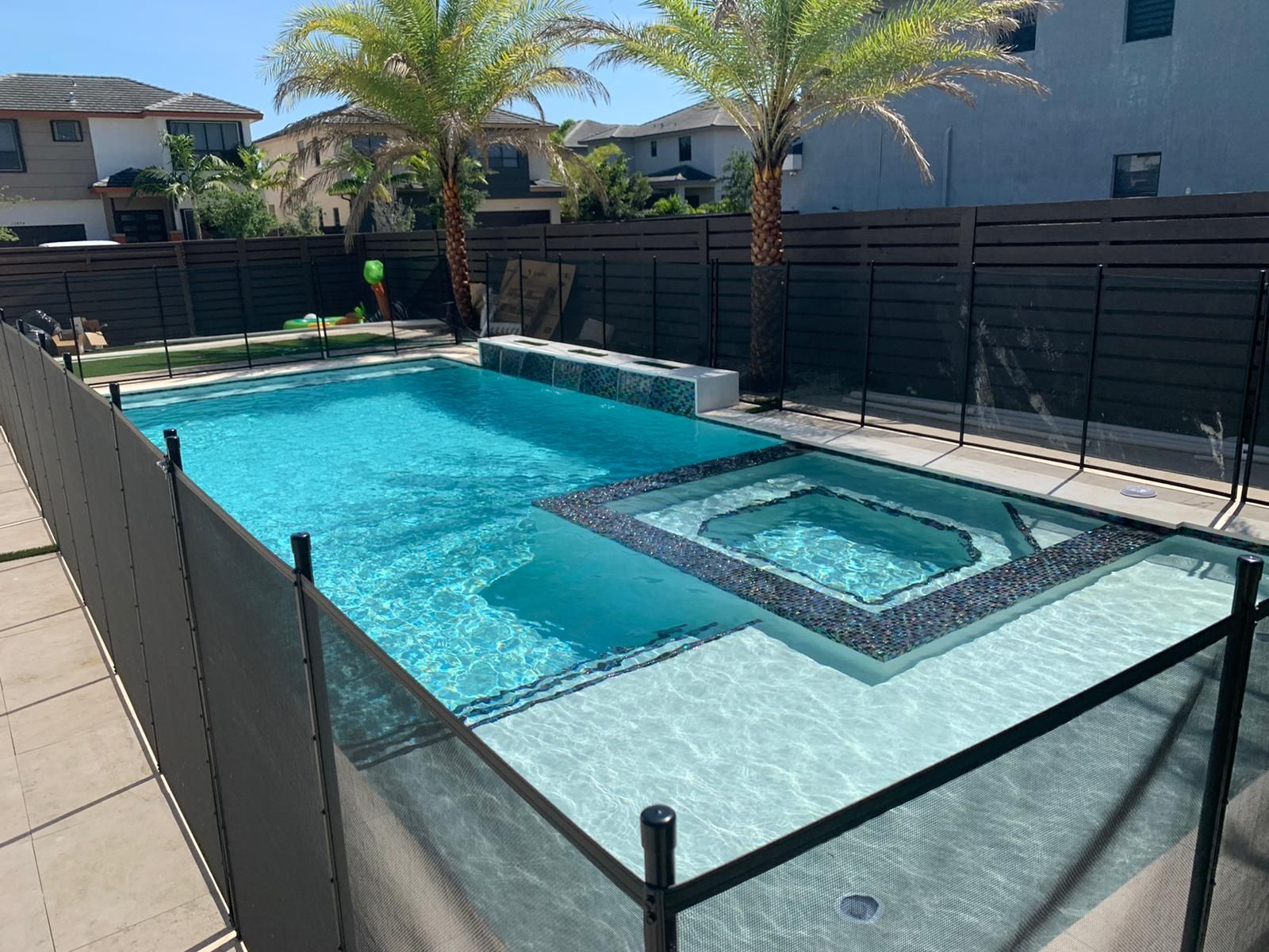 A large swimming pool surrounded by a fence and a hot tub.