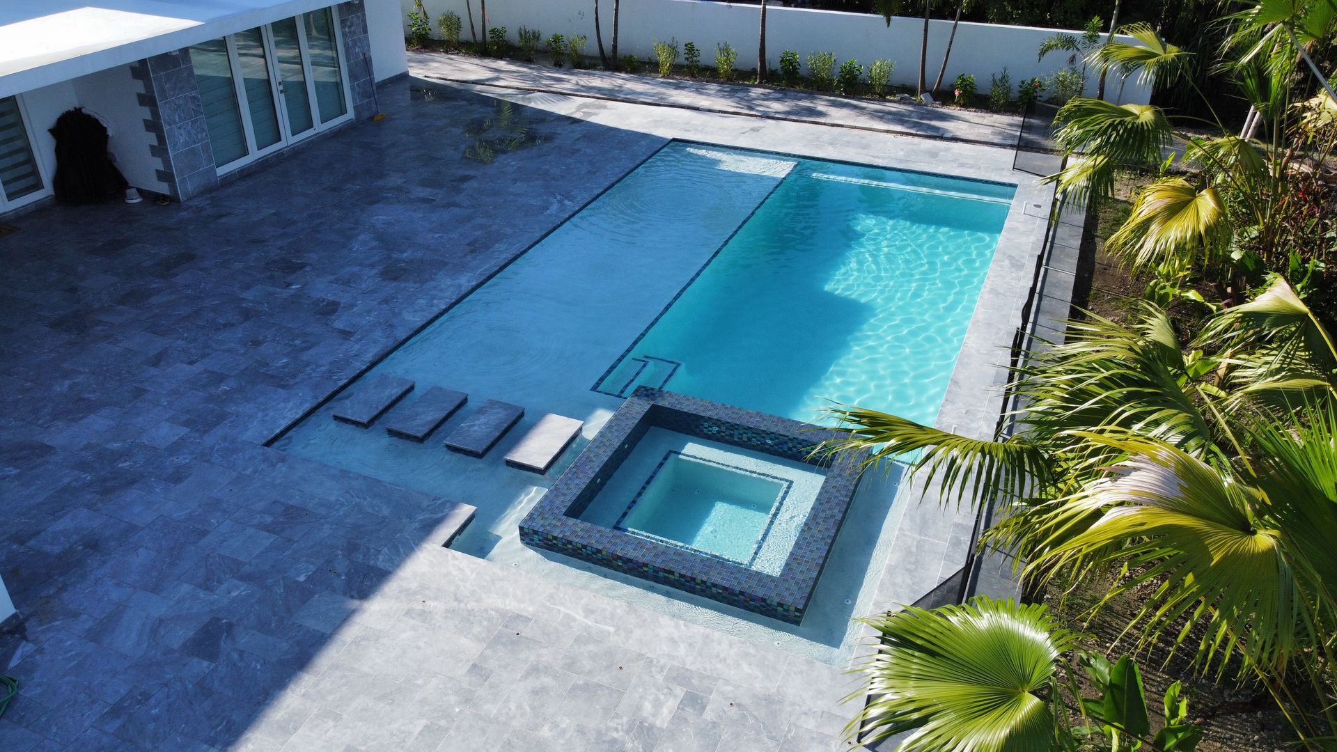 A large swimming pool with a hot tub in the backyard of a house.