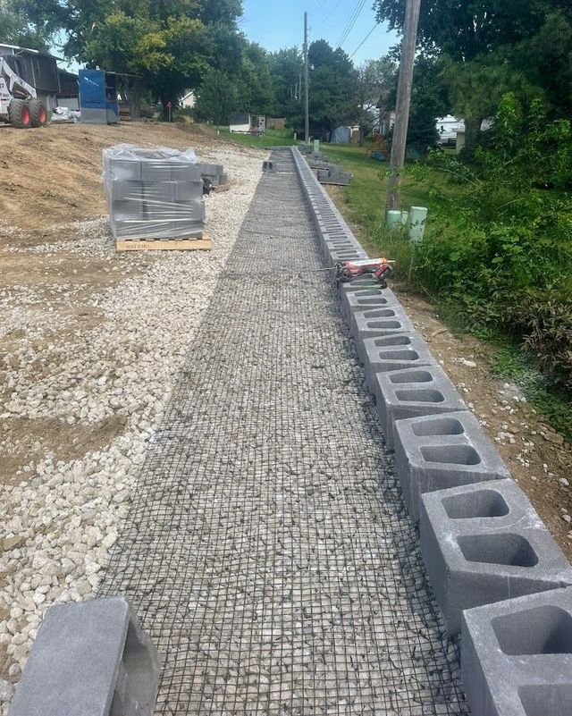 Construction site: cinder block retaining wall under construction along gravel path.