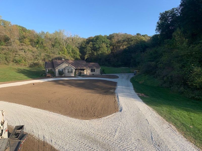 House nestled in a wooded area with gravel driveway and newly seeded lawn.