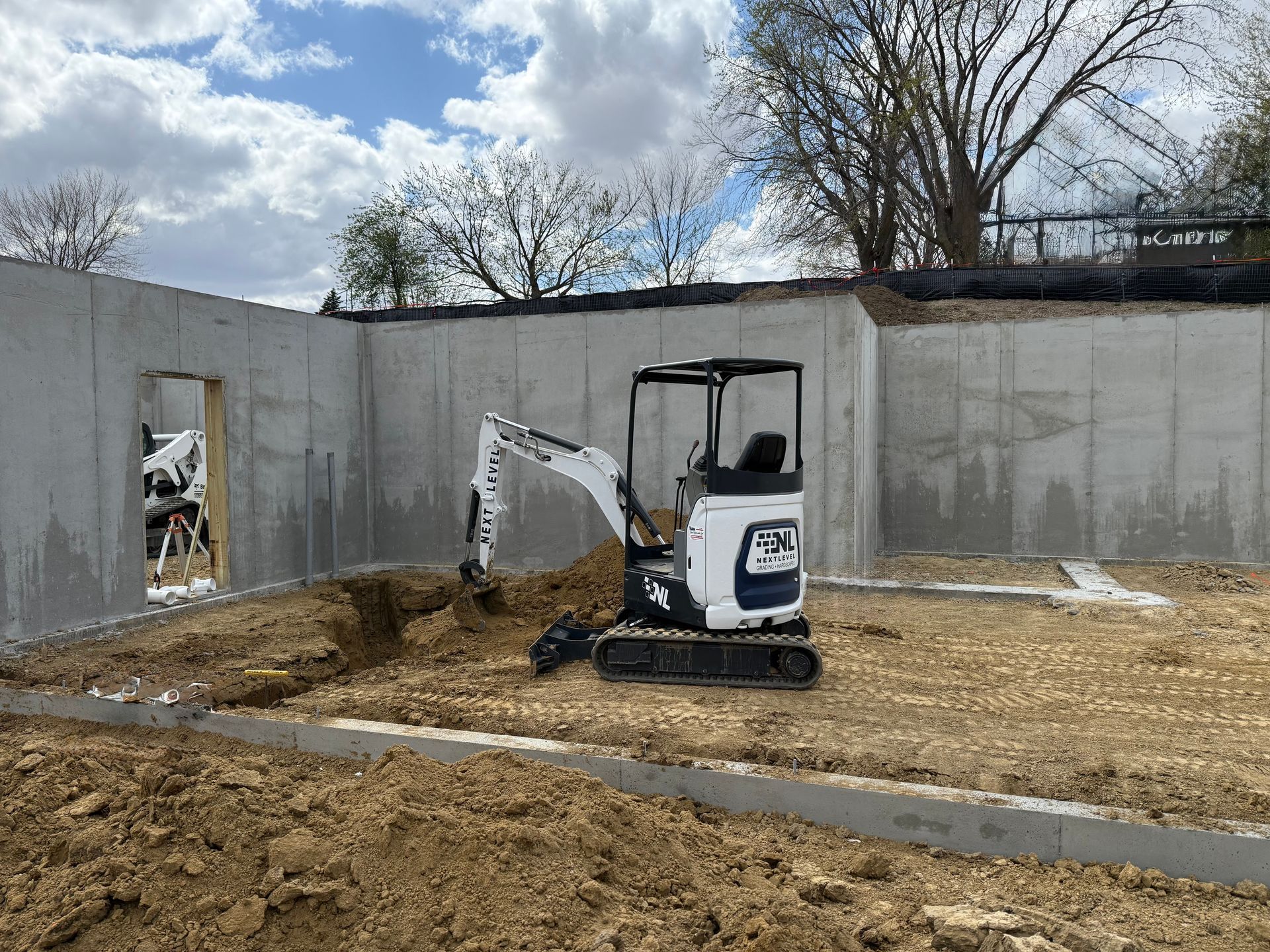 Mini excavator in a concrete structure, digging in dirt, under a cloudy sky.