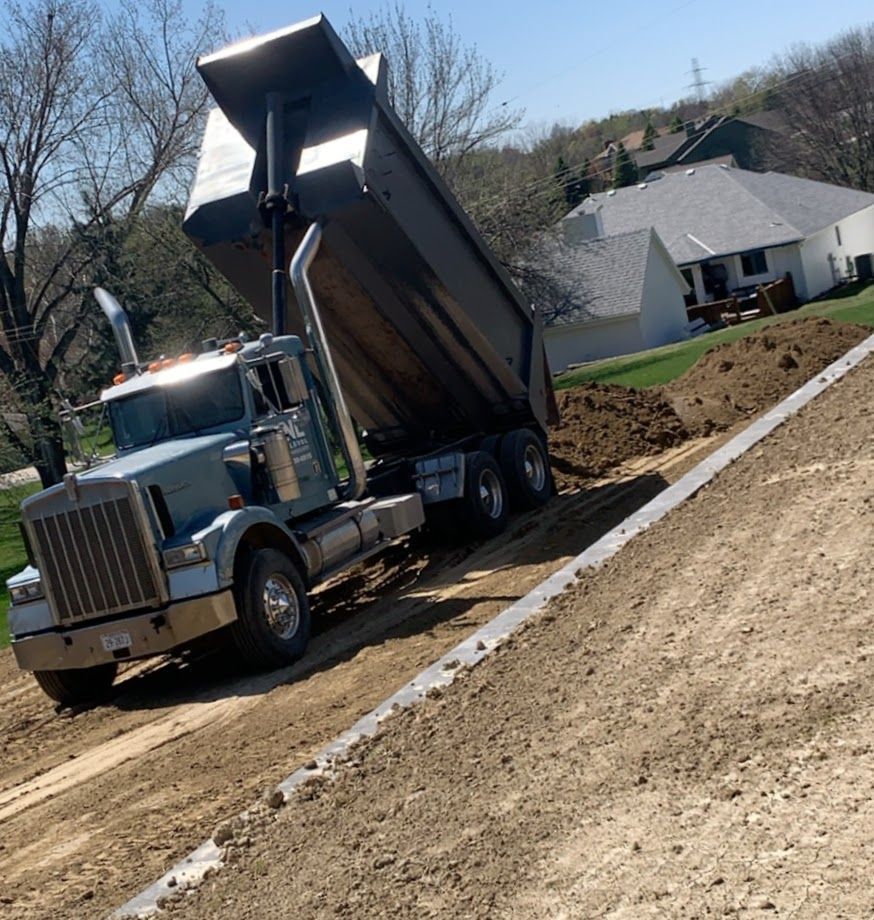 Dump truck unloading soil near a residential house with a gray roof and a green lawn.