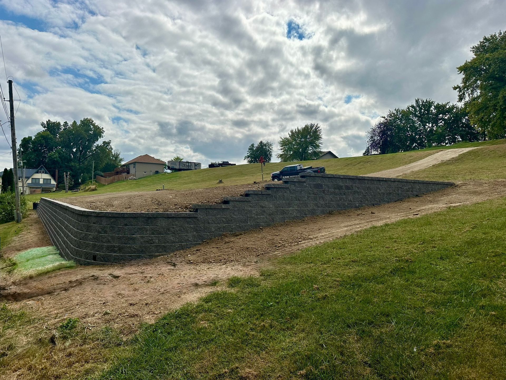 Retaining wall construction on a grassy hillside under a cloudy sky.