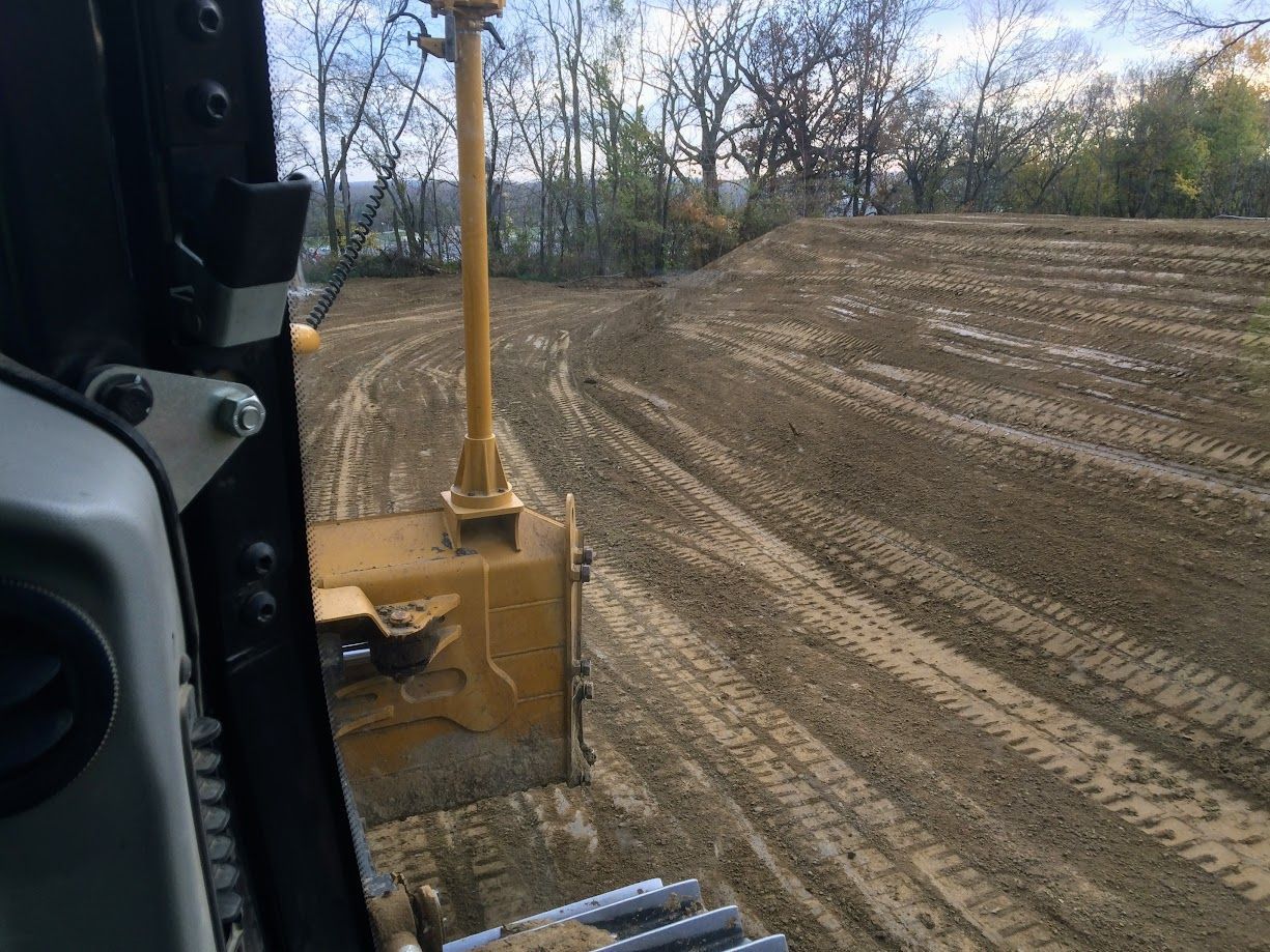 View from bulldozer cab grading a muddy field, trees in the background.