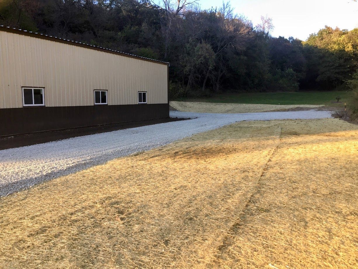 Exterior view of a beige building with gravel and grass areas; trees and sky in the background.
