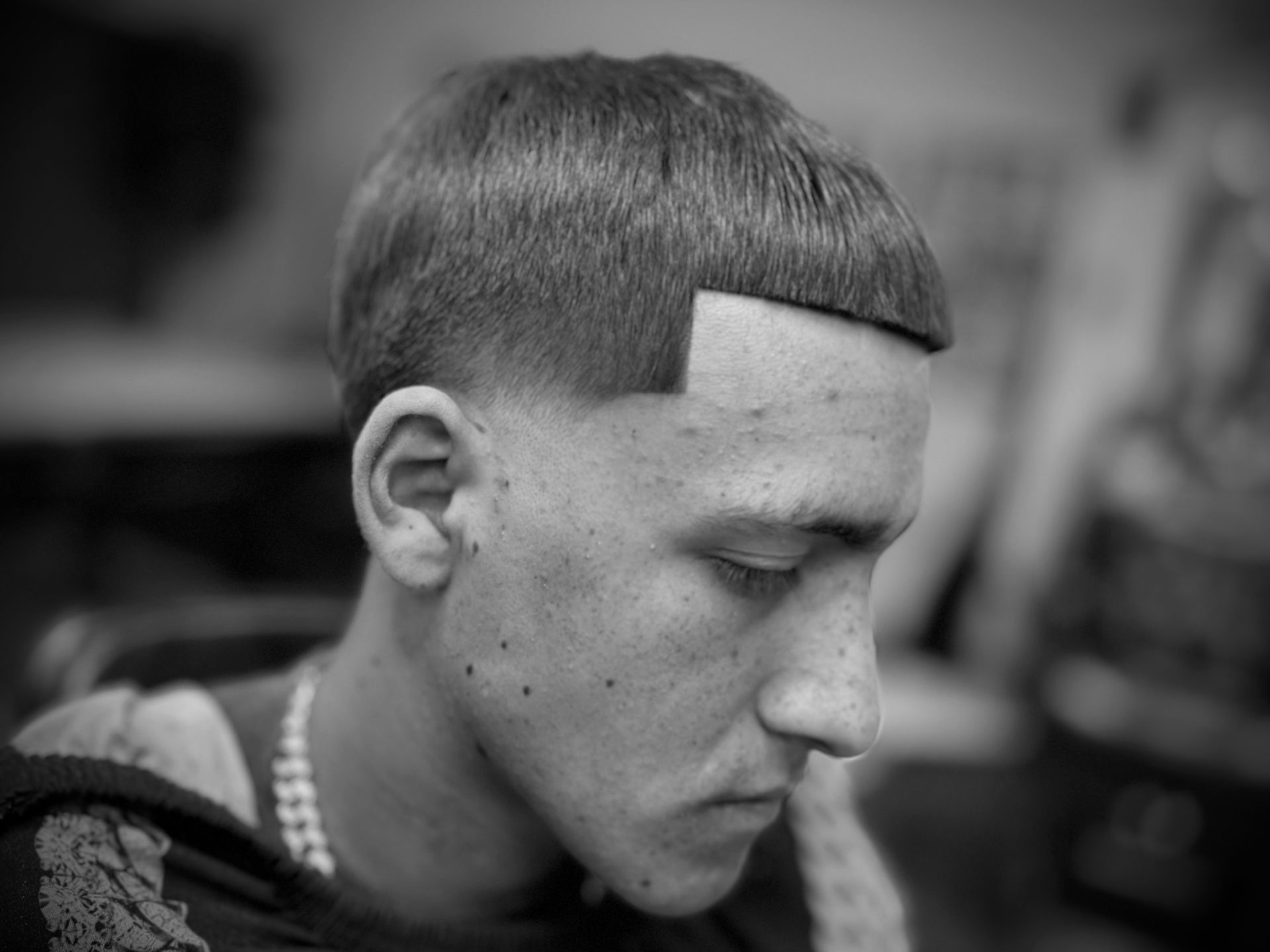 Man with a short haircut, faded sides, looking down. Black and white.