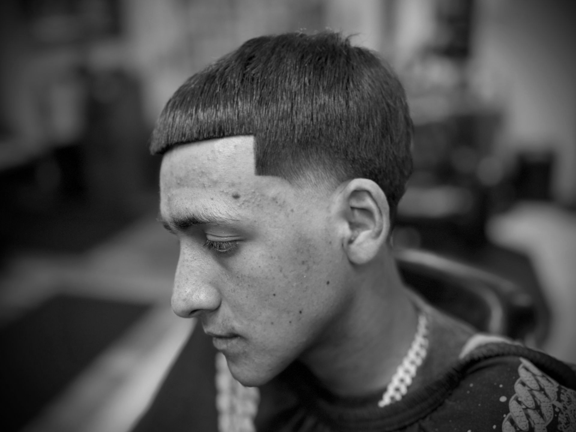 Man with short haircut, clean sideburn, looking down, in a barber shop setting.