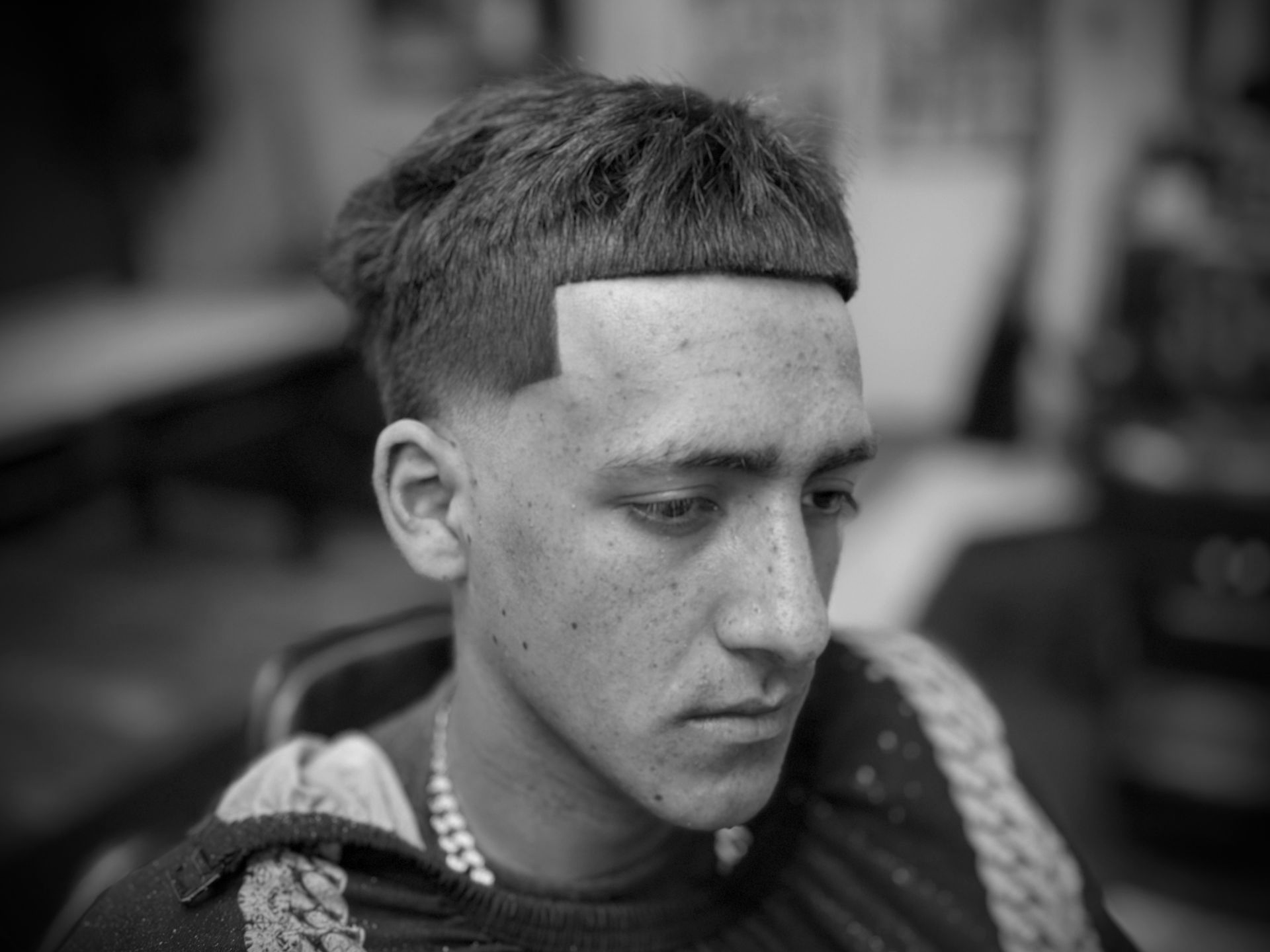 Man with sharp haircut, looking down, in a salon. Black and white photo.