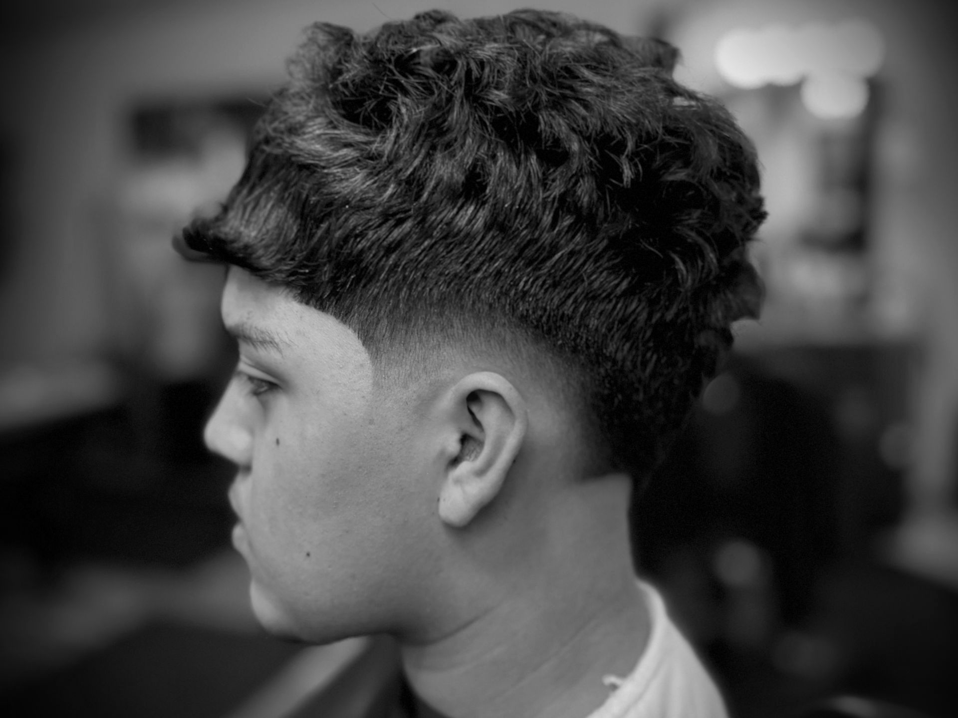 Man with a high fade haircut, dark curly hair on top, side profile.