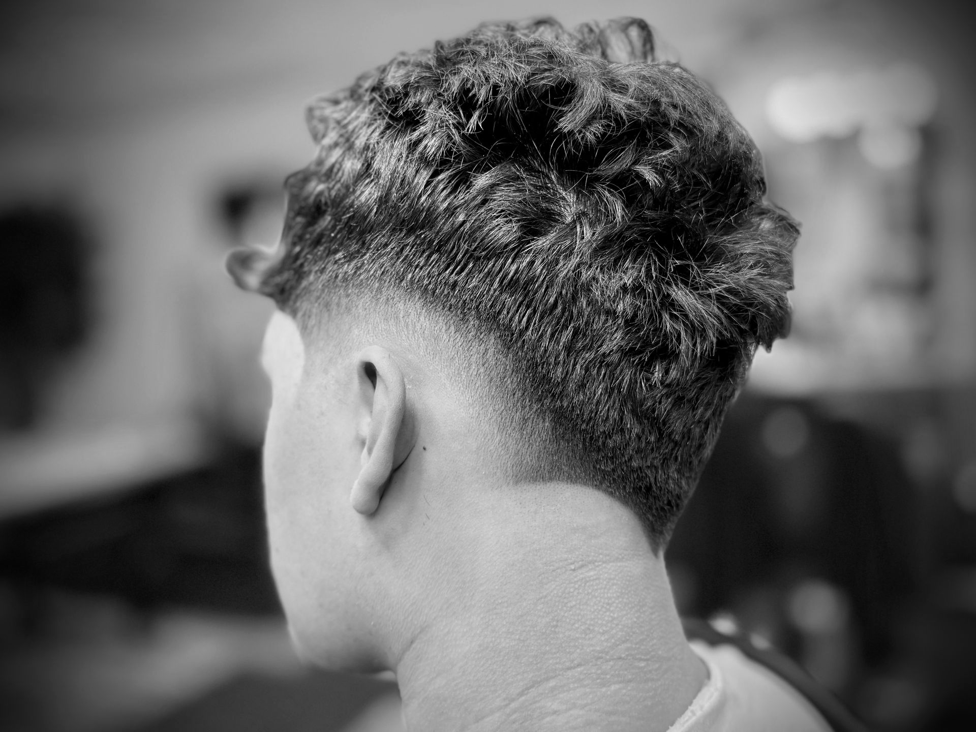 Man's head, showing a fade haircut. The hair is dark and textured on top, with a cleanly shaved neckline.