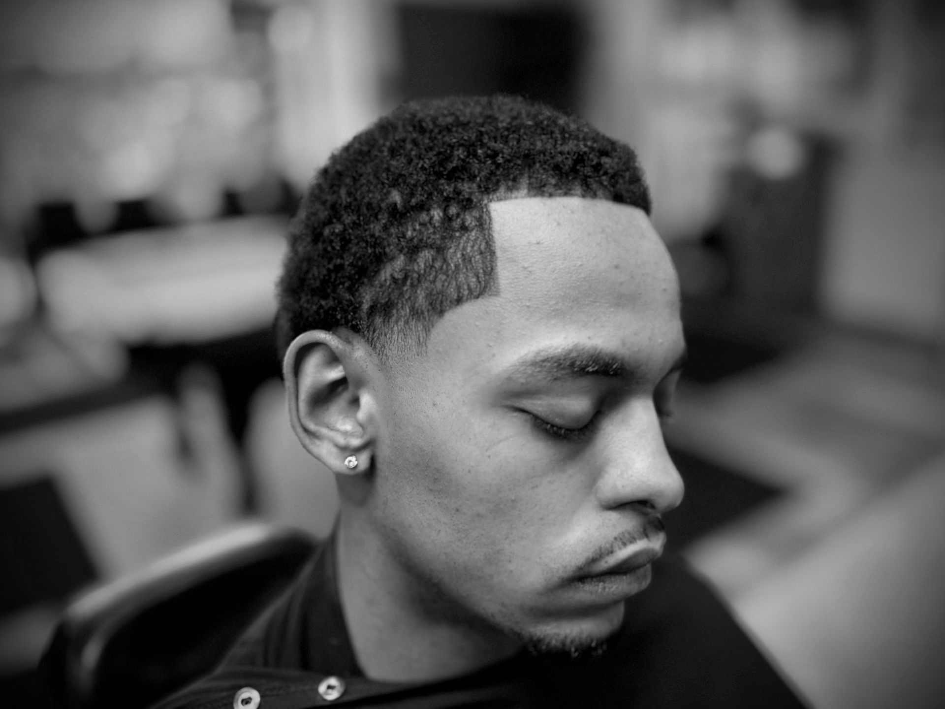 Man with a neatly trimmed fade haircut, eyes closed, in a barber shop.
