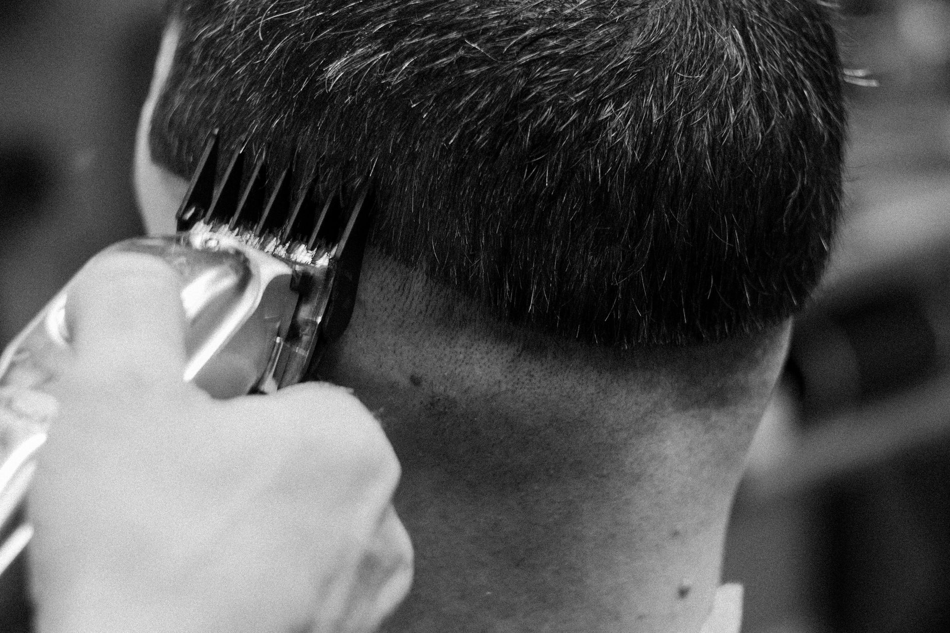 Hair clipper cutting a person's hair on the back of their neck, black and white.