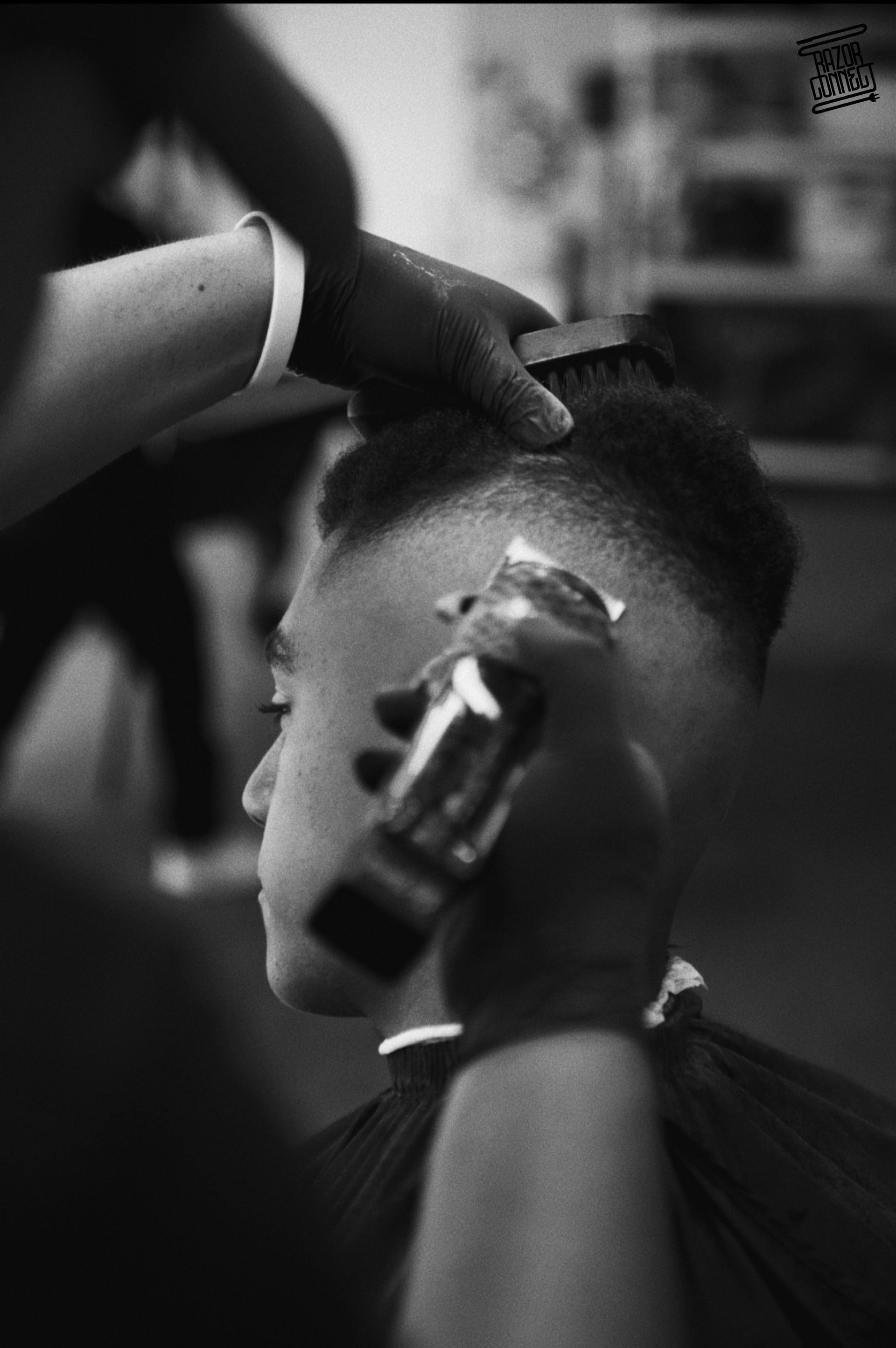 Barber giving a fade haircut, using clippers and brush. Black and white photo.