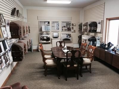 Interior of a showroom with caskets displayed on walls, a table, chairs, and office equipment.