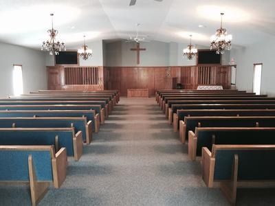 Interior of a church sanctuary with rows of pews, wooden altar and cross, chandeliers, and two large screens.