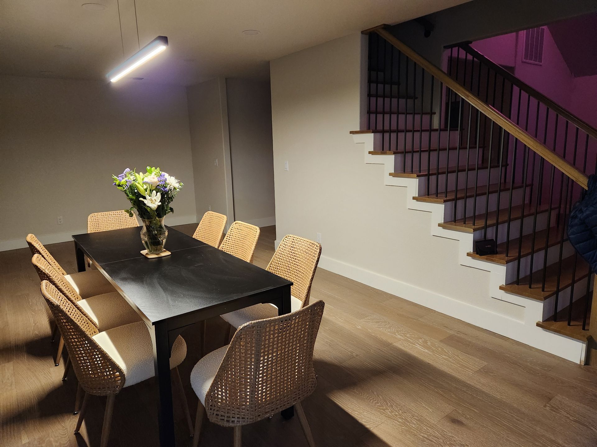 Dining room with a black table, wicker chairs, and stairs with a black railing.