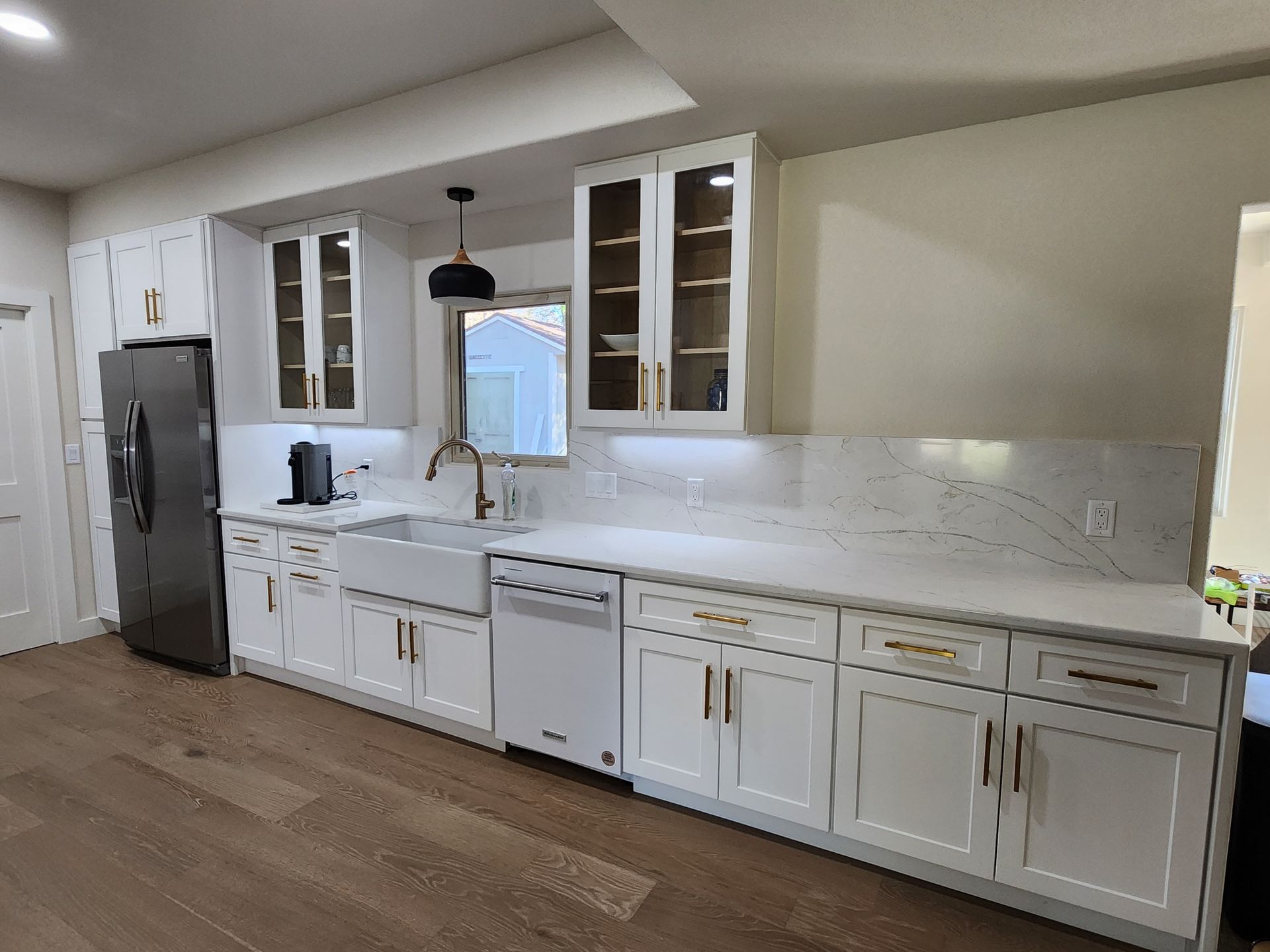 Modern white kitchen with light countertops, stainless steel fridge, and wood floors.