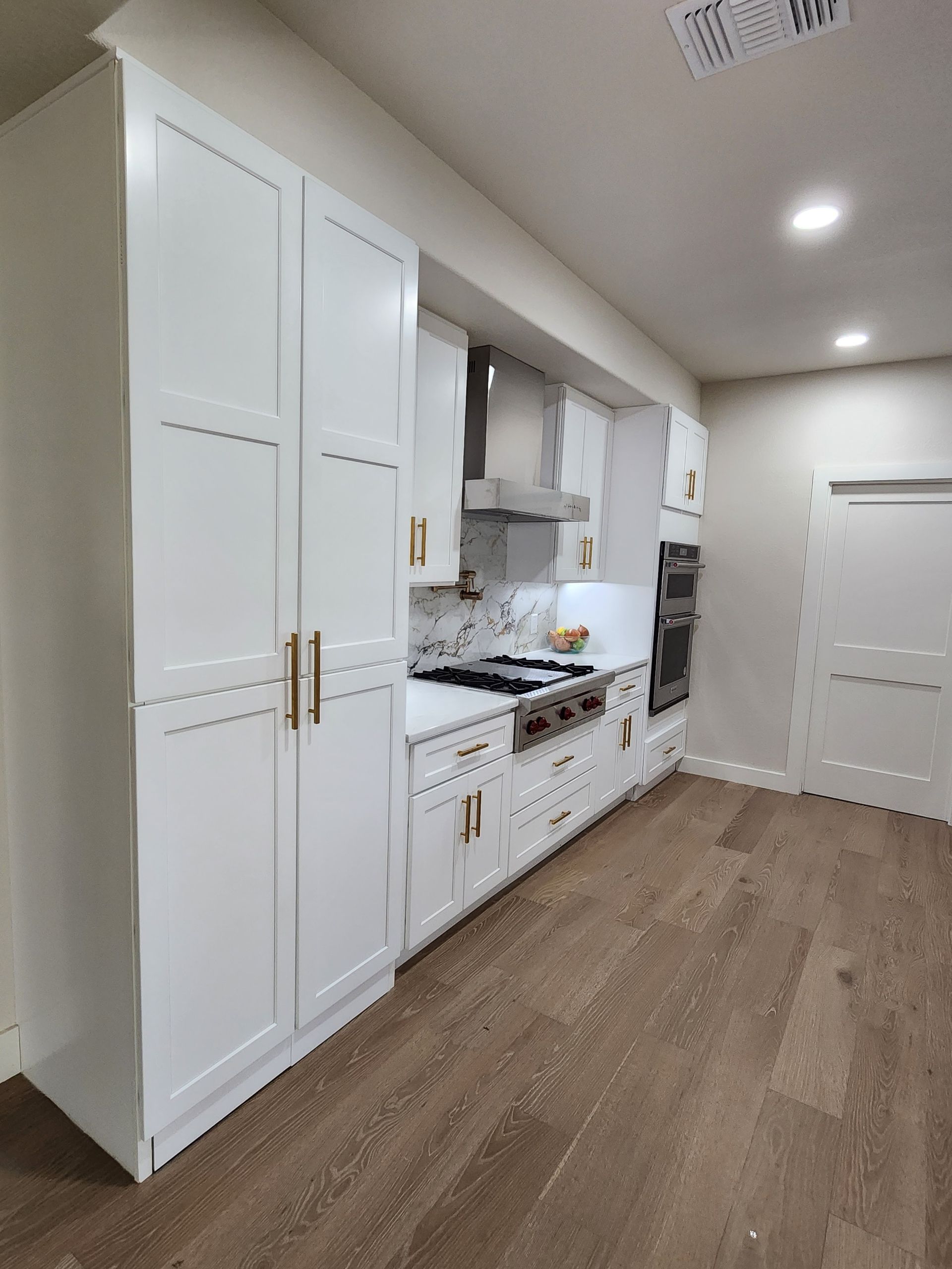 White kitchen with wood floors and gold hardware.