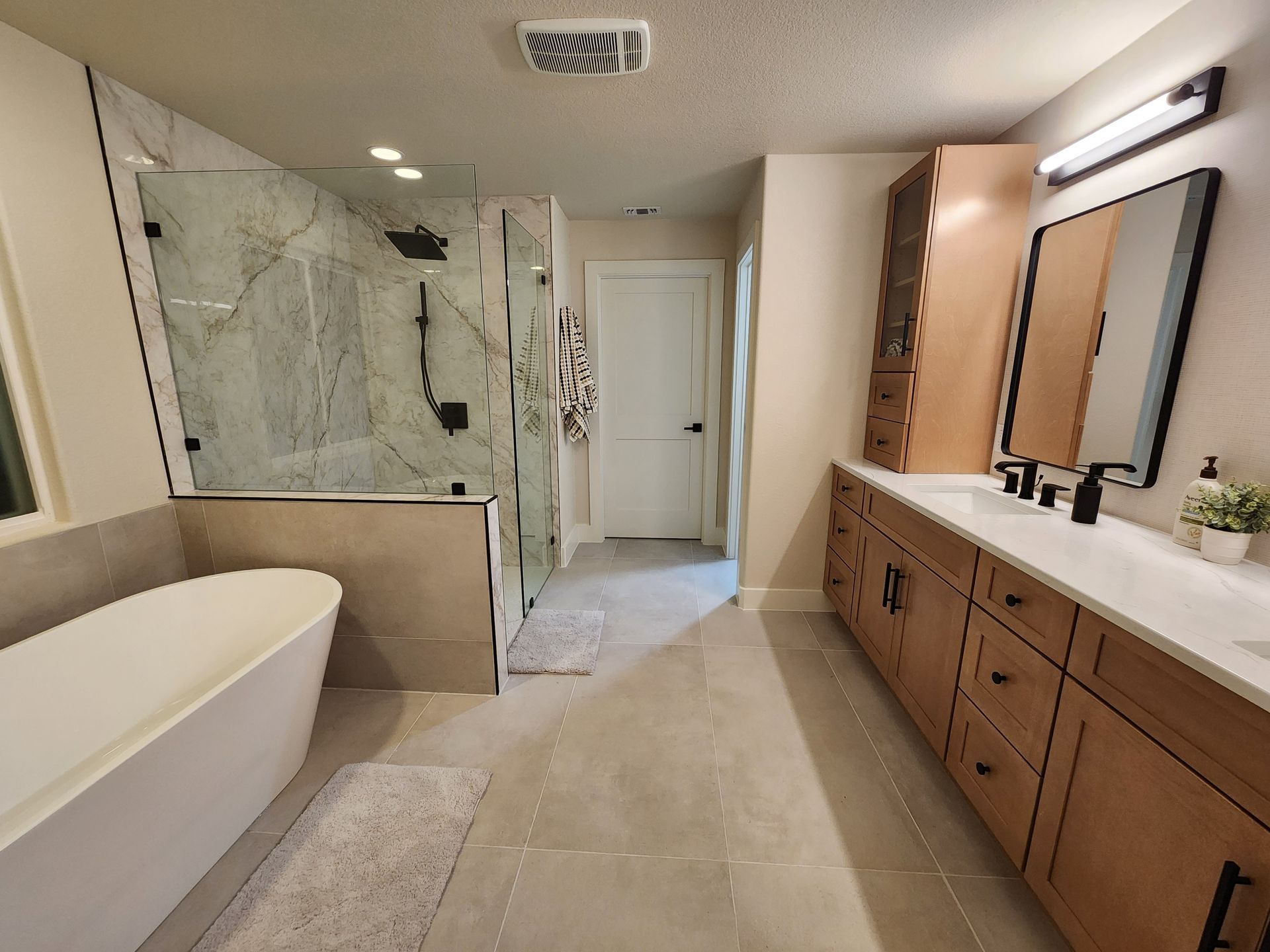 Modern bathroom with a freestanding tub, glass shower, wood vanity, and marble tile.