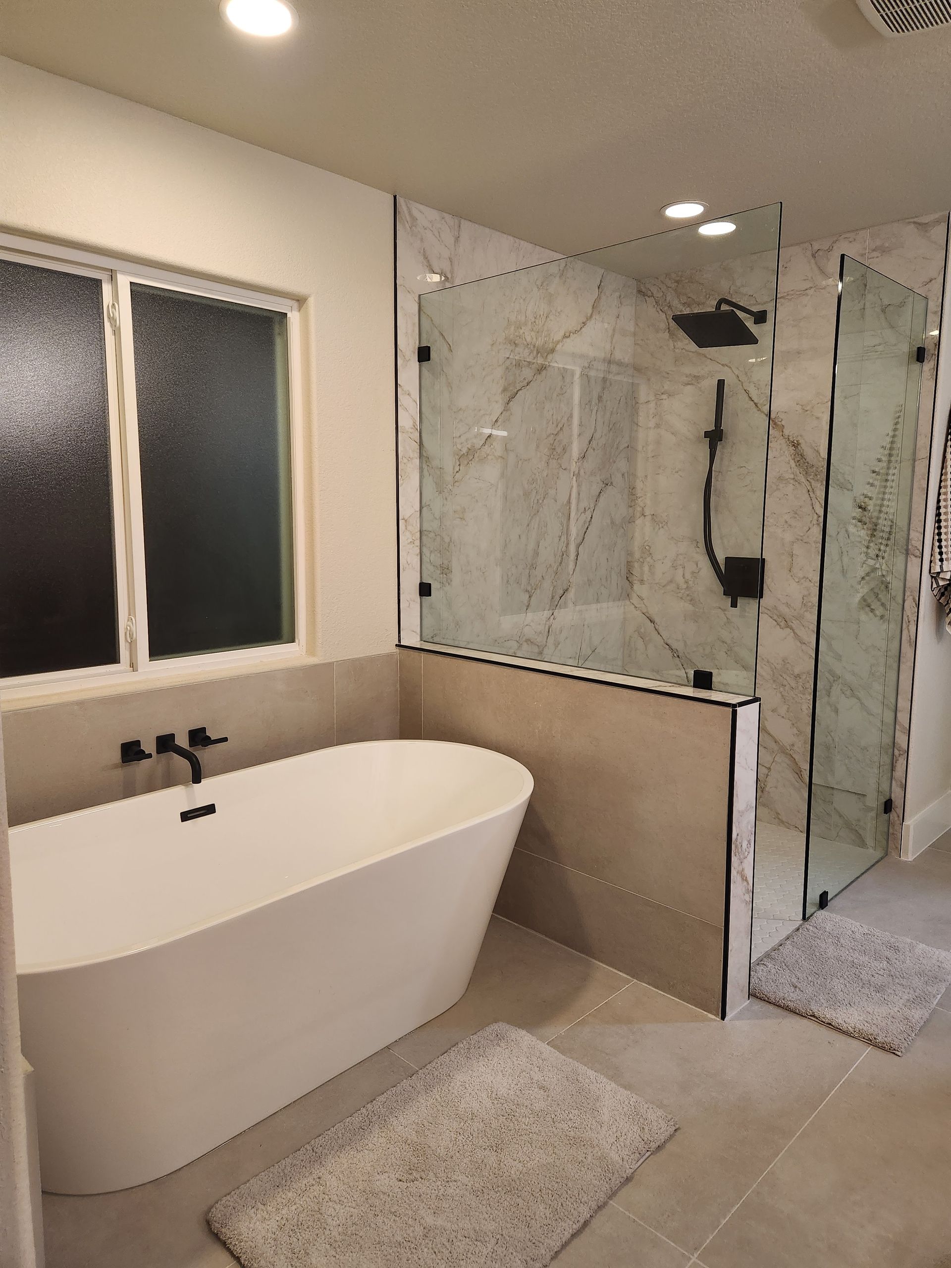 Modern bathroom with a white soaking tub, glass shower, and window. Gray and white tones.