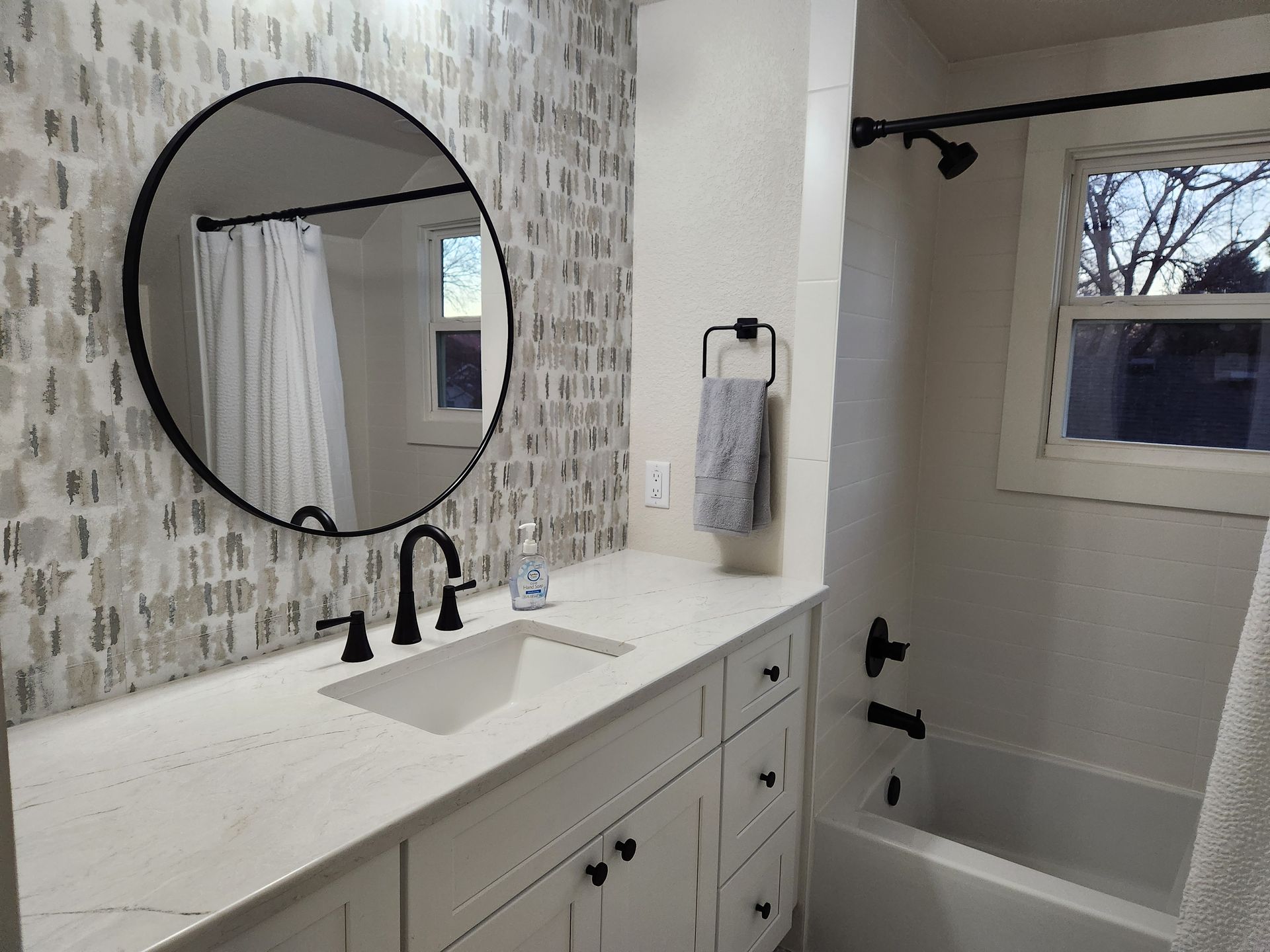 Bathroom with white countertop, black fixtures, and patterned tile backsplash.
