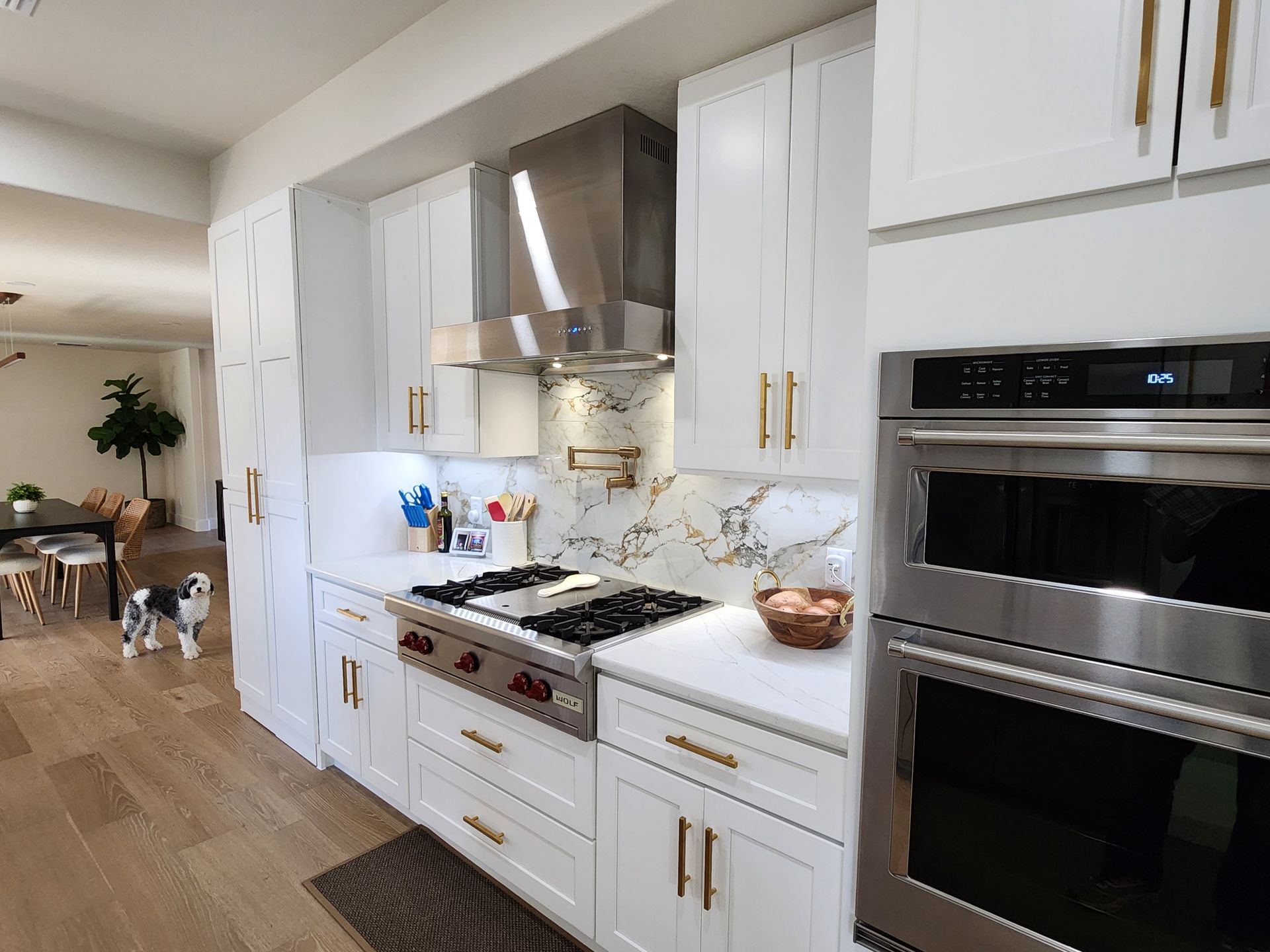 White kitchen with stainless steel appliances, white cabinets, and a marble backsplash.