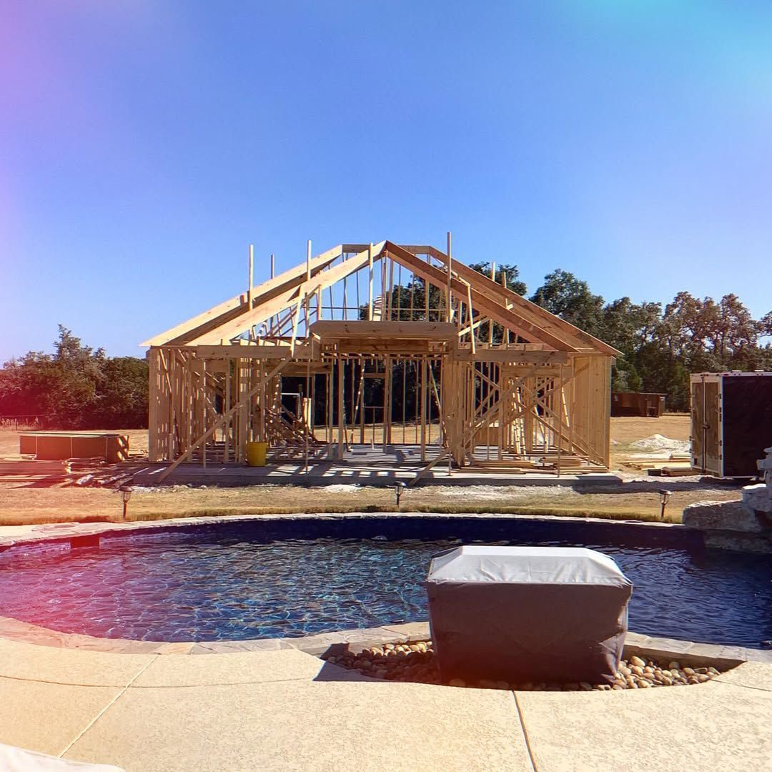 Wooden frame of a house being built next to a swimming pool on a sunny day.