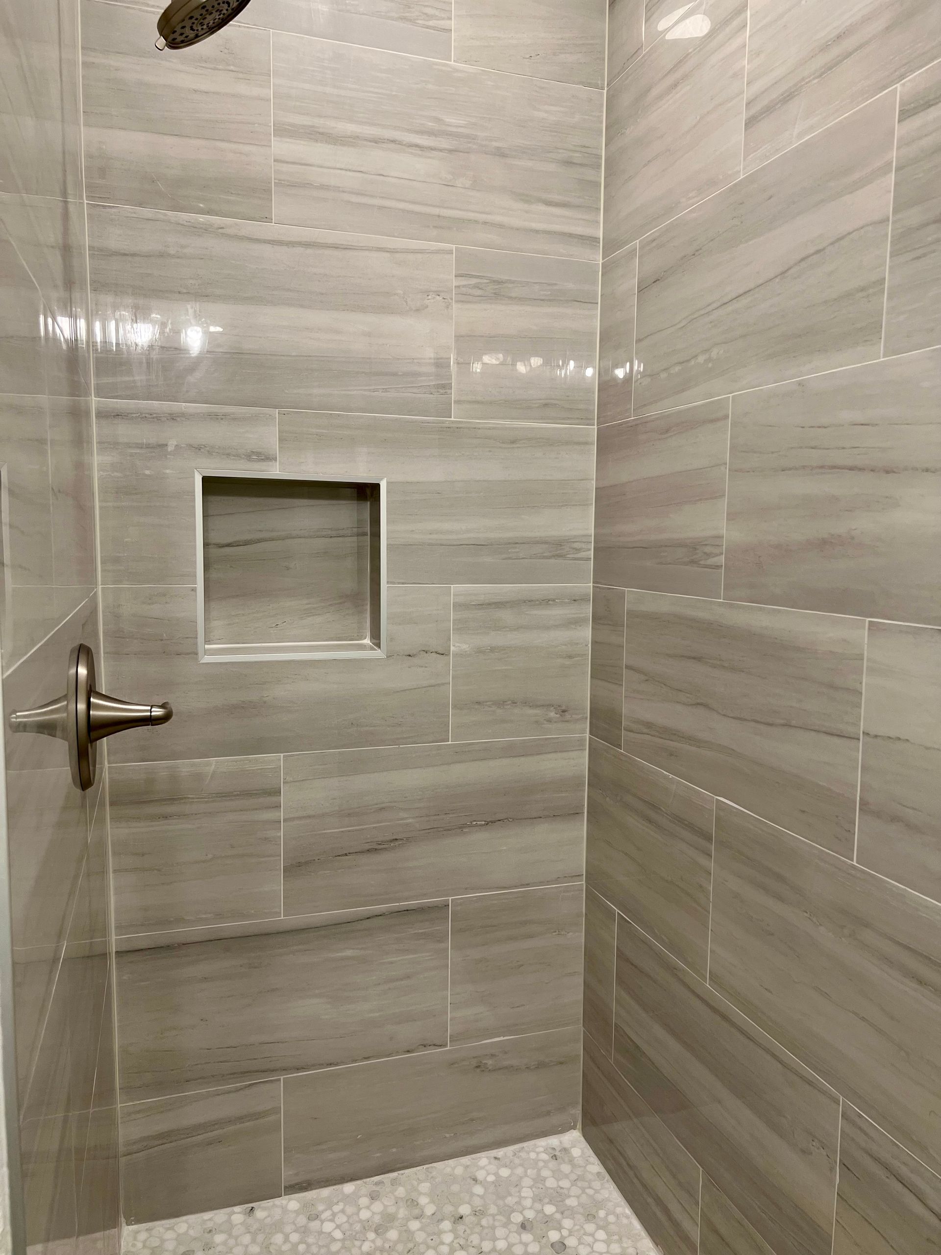 Shower with gray and white stone tiles, a built-in shelf, and bronze fixtures.